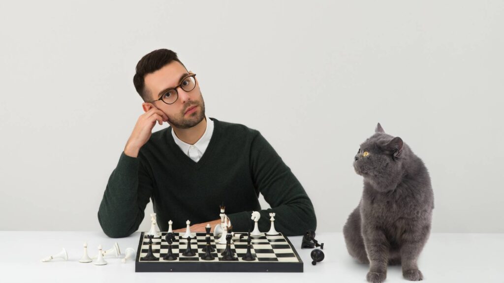 man with a chesss table and a cat right next to it, learning from the expert how to outsmart mice