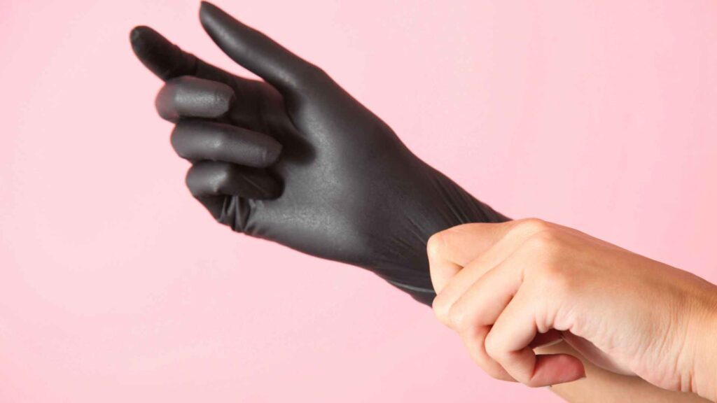 hands with black gloves over a pink background to illustrate the caution you need for DIY old house borer treatment