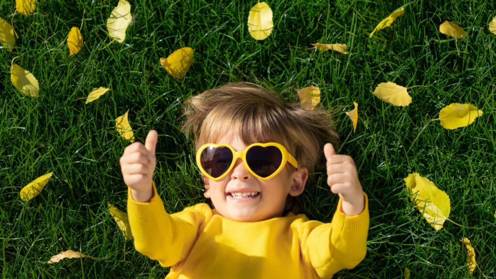 kid with a yellow shirt and yellow sunglasses laying on the grass enjoying the freedom after quick flea treatment for house